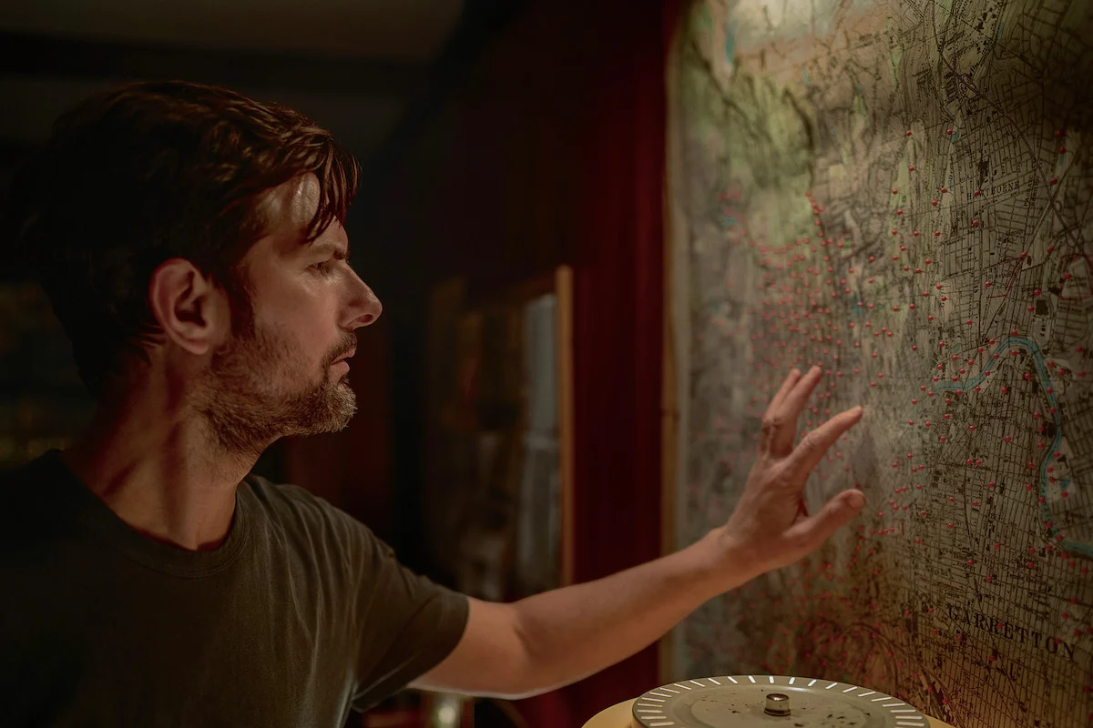 Adam Scott diante de um mapa cheio de marcações em O Homem que Sussurra
