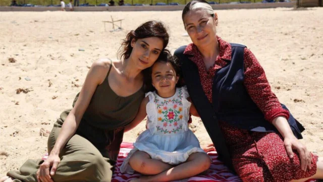 Duas mulheres e uma menina sentadas juntas em uma área externa em Mãe