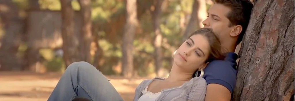 Emir e Feriha estão sentados juntos junto a uma árvore em cena de O Segredo de Feriha