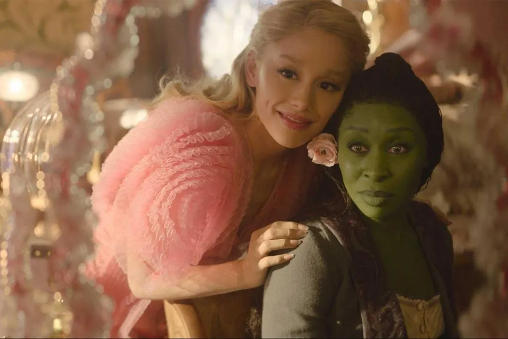 Glinda apoia a cabeça no ombro de Elphaba em um campo florido durante Wicked.
