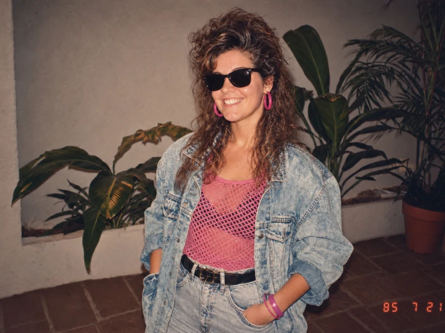 Mulher com jaqueta jeans, óculos escuros e acessórios rosa em imagem inspirada nos anos 80 do ChatGPT