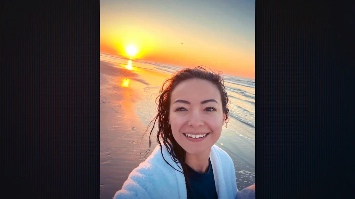 Mica Miller sorrindo em selfie na praia ao nascer do sol