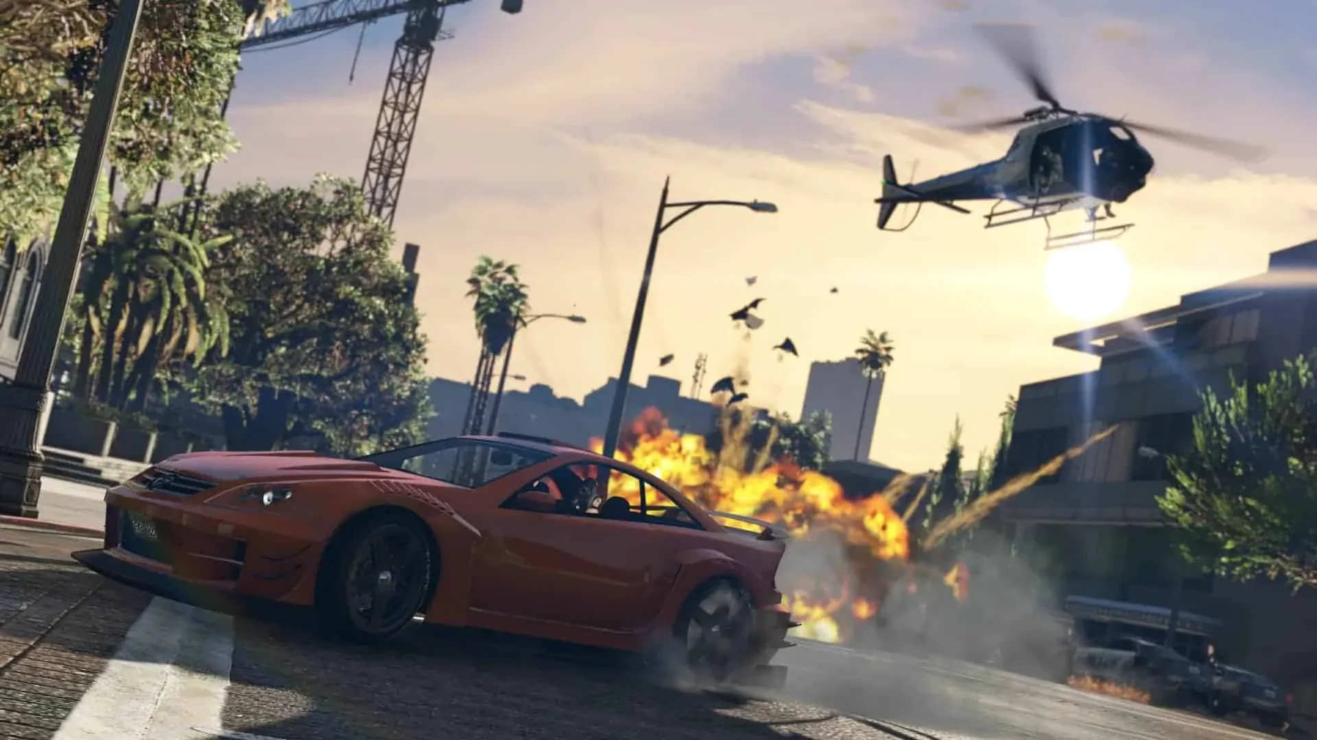 Carro vermelho faz uma curva diante de uma explosão, com um helicóptero ao fundo, em GTA Online.