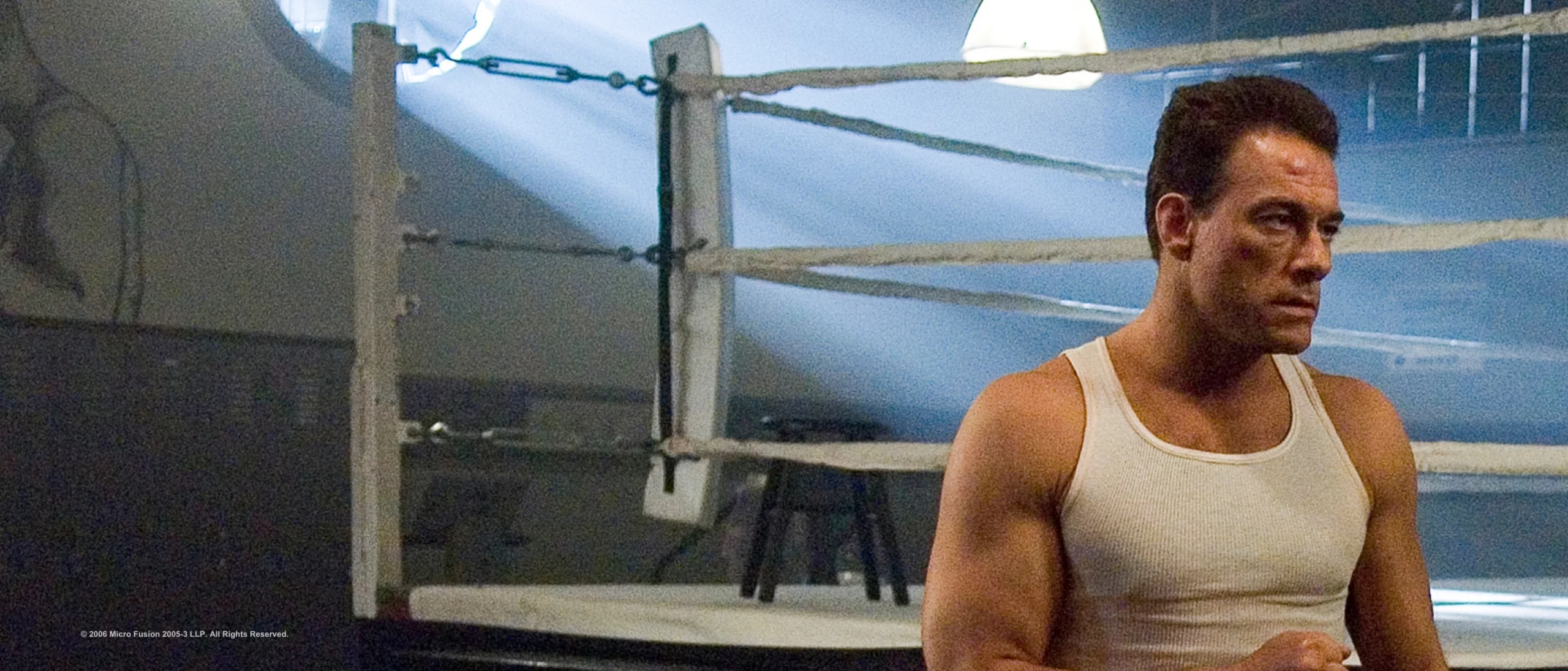 Jean-Claude Van Damme de regata branca, junto a um ringue de boxe, em Força de Proteção
