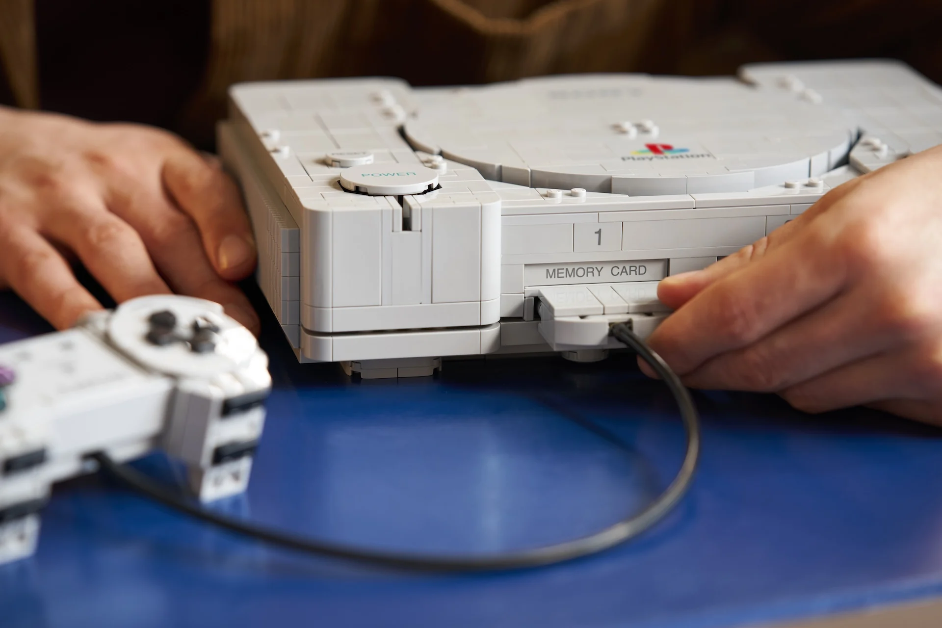 Pessoa conectando o controle construído com LEGO à entrada frontal do LEGO PlayStation