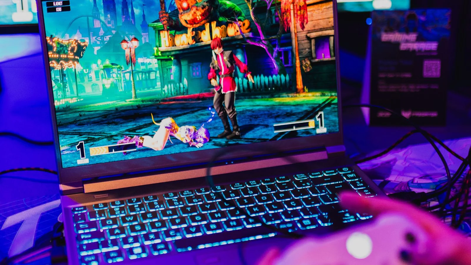 Pessoa jogando em notebook com controle enquanto uma partida aparece na tela
