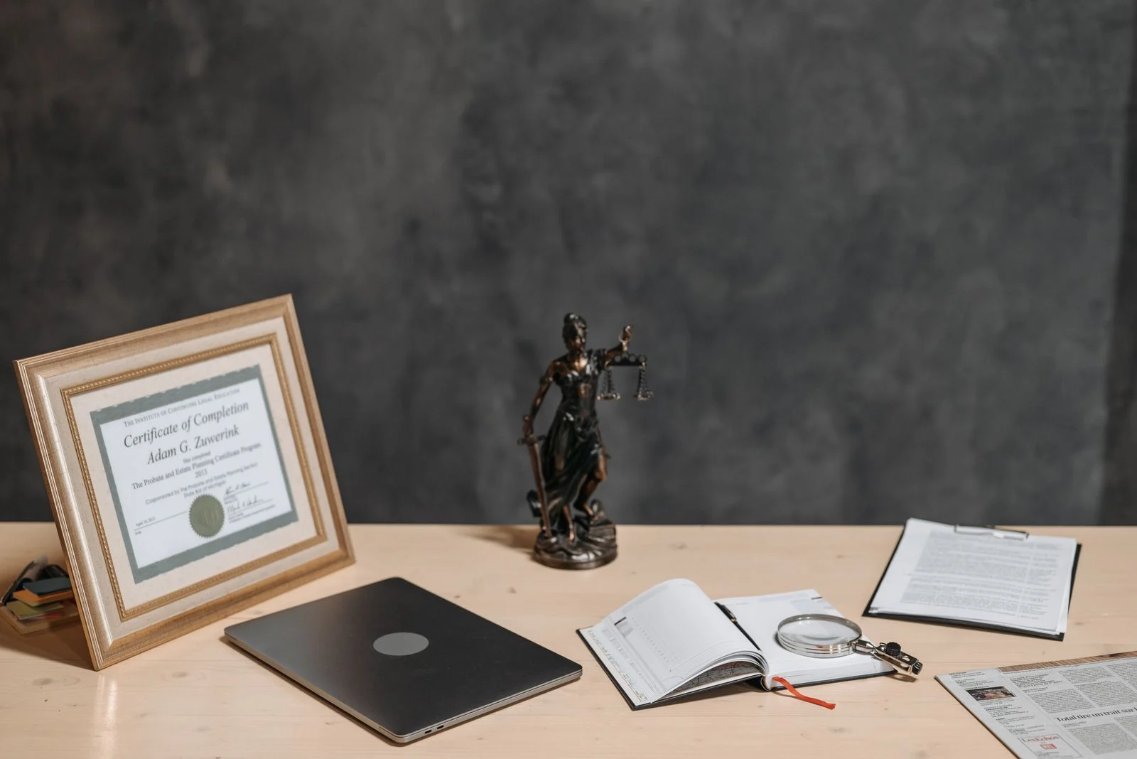 Mesa de trabalho jurídico com notebook, documentos, lupa e estátua da Justiça