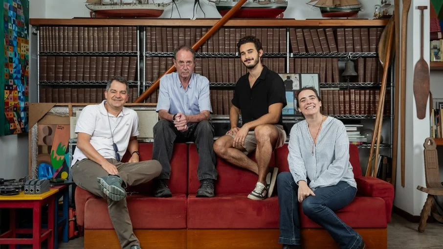 Integrantes da produção de 100 Dias reunidos em ambiente com livros e objetos náuticos durante divulgação do filme
