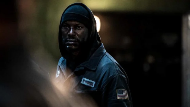 Tyrese Gibson interpreta Mercer, de capuz e uniforme de fábrica, em uma cena escura do filme 1992