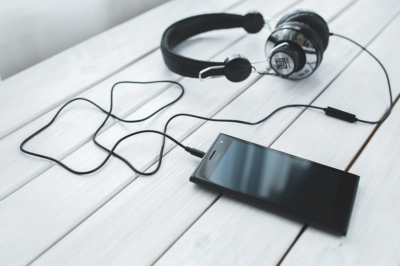 Fone de ouvido ligado a celular sobre mesa clara, ilustrando a escuta de músicas sem internet