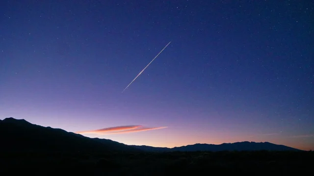 Meteoro das Orionídeas corta o céu antes do amanhecer, acima de montanhas em uma fotografia de 2025