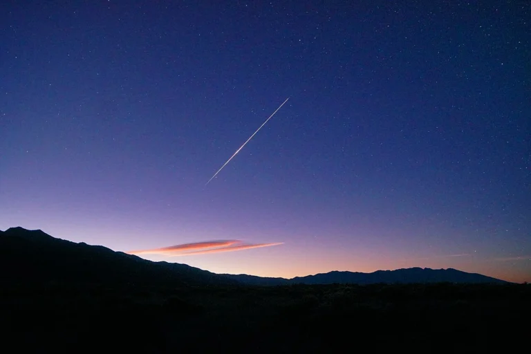 Meteoro das Orionídeas corta o céu antes do amanhecer, acima de montanhas em uma fotografia de 2025