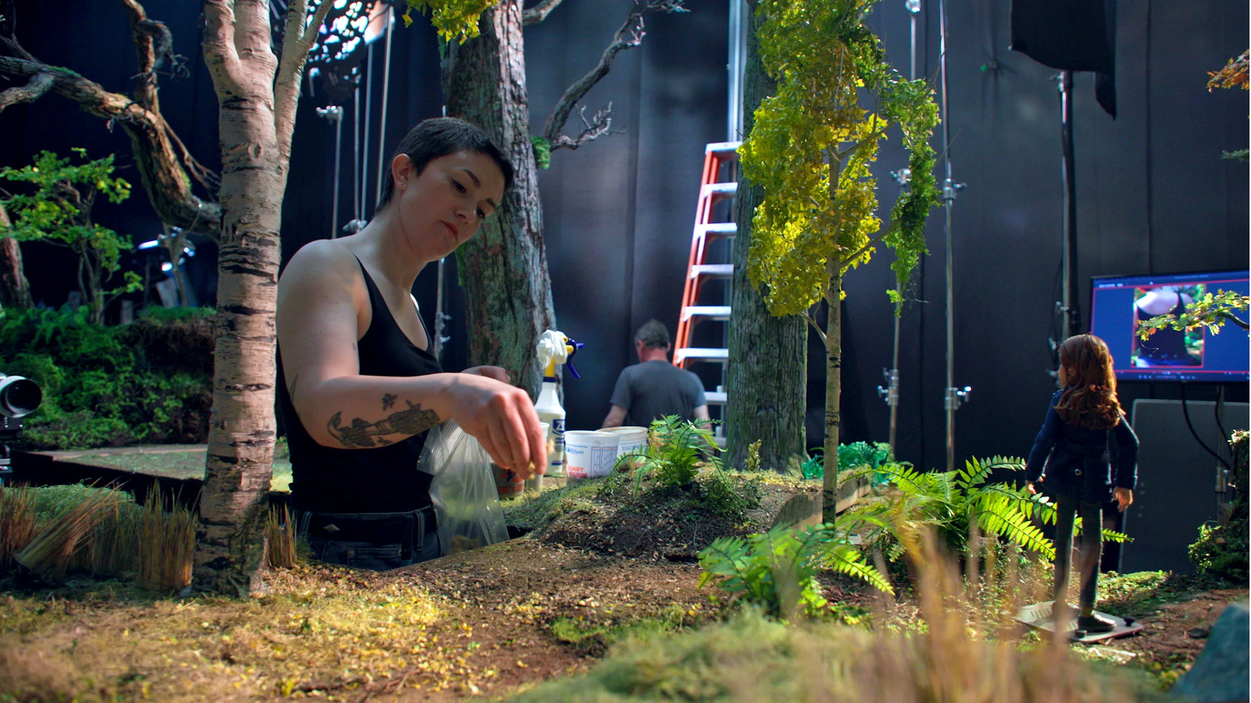 Artista da LAIKA posiciona plantas em miniatura em um cenário florestal construído para O Bosque Selvagem