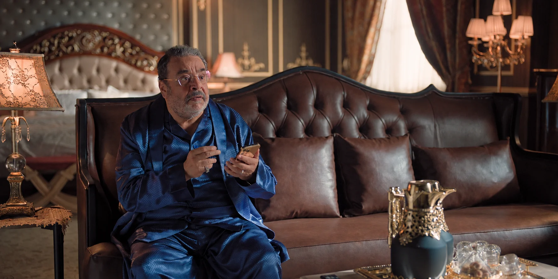Sultan segura um celular enquanto está sentado em um sofá em Ricos Sem Dinheiro