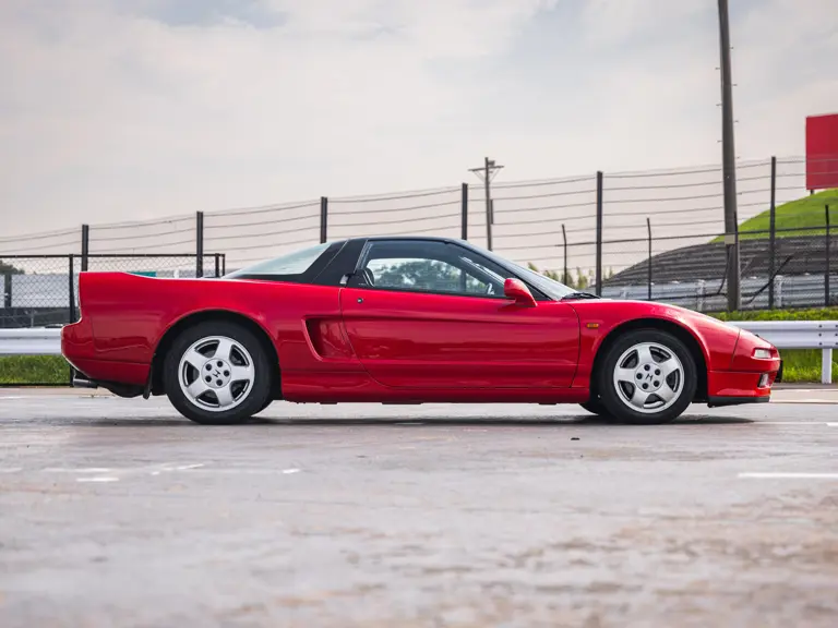 Honda NSX vermelho de Ayrton Senna visto de perfil, mostrando o teto preto, as rodas originais e a carroceria baixa
