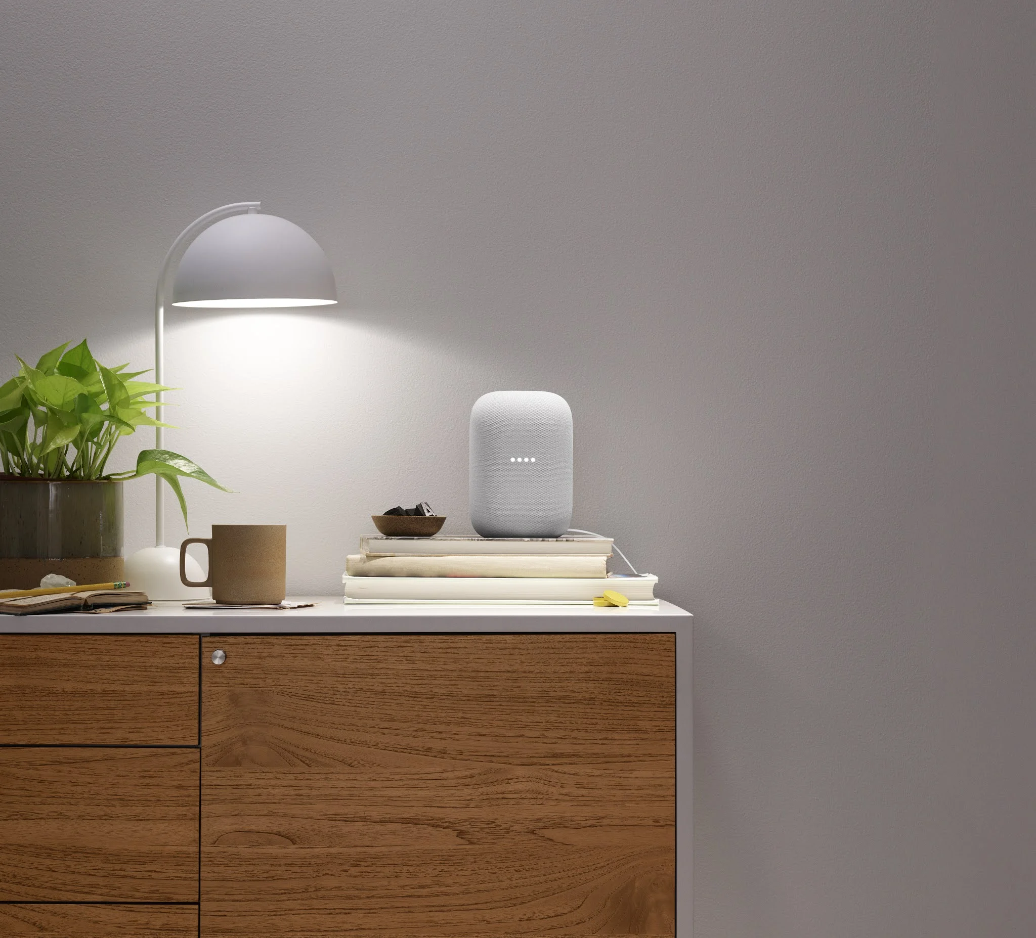 Alto-falante Google Nest Audio cinza sobre móvel de madeira com luminária acesa ao lado