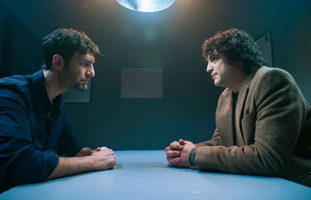 Devran, personagem de Aras Bulut İynemli em Deha, conversa com outro homem em uma sala pouco iluminada
