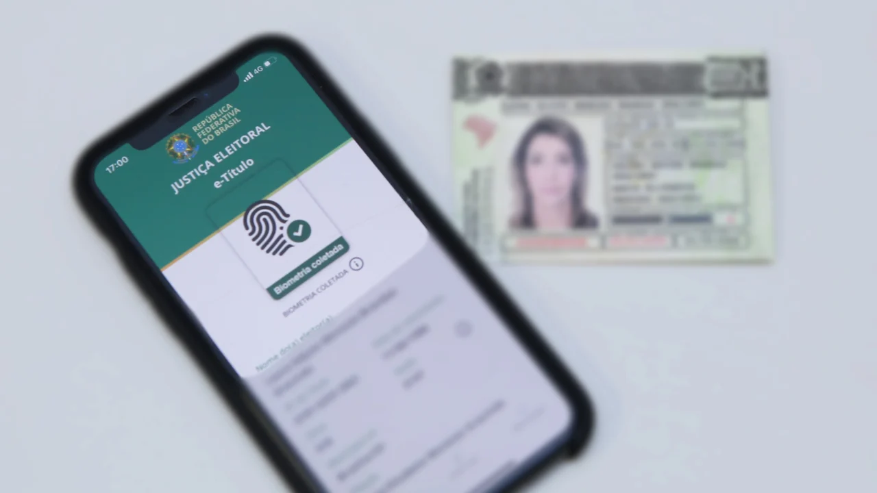 Celular com o e-Título e indicação de biometria cadastrada diante de um documento de identidade.