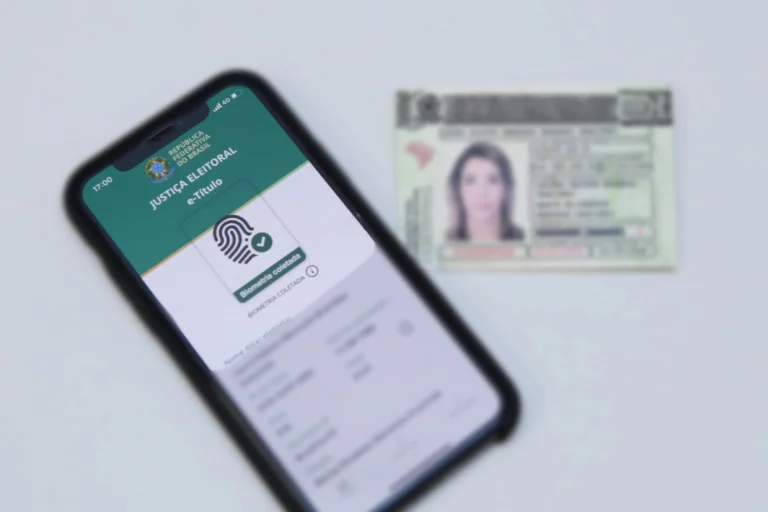 Celular com o e-Título e indicação de biometria cadastrada diante de um documento de identidade.