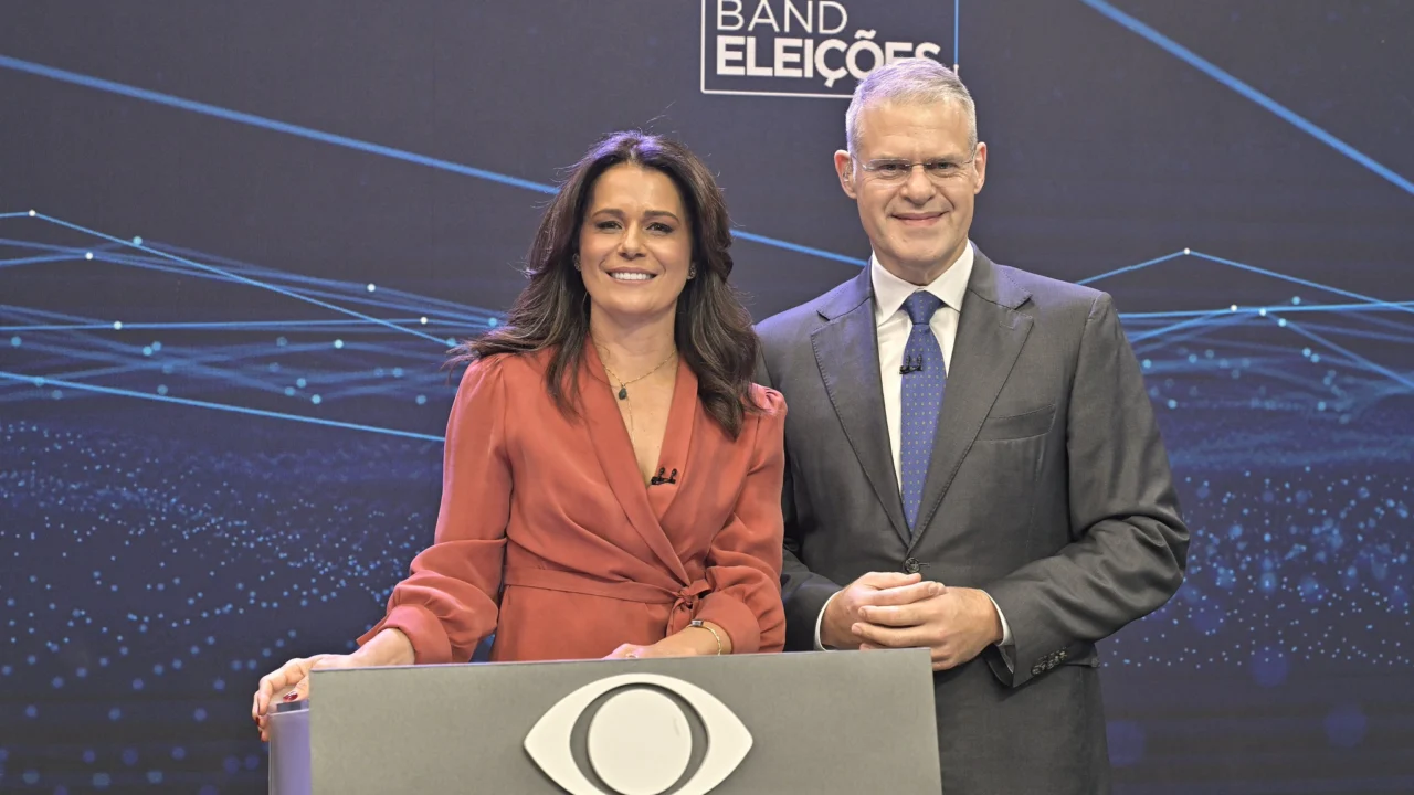 Adriana Araújo e Eduardo Oinegue diante do cenário Band Eleições, mediadores do debate presidencial.