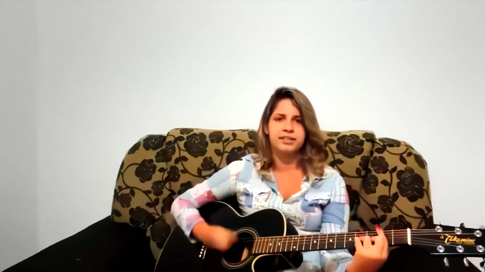 Marília Mendonça jovem toca violão sentada em um sofá, em registro de arquivo de Sentimento Louco