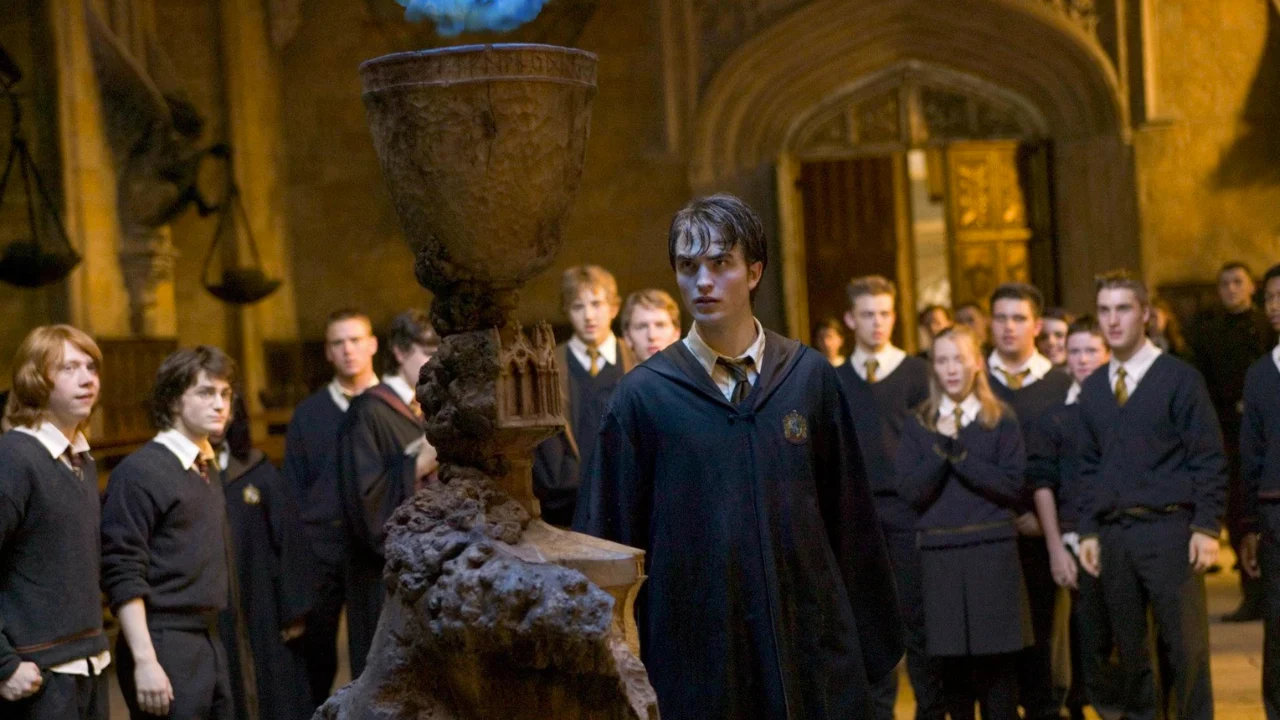 Cedrico Diggory diante do Cálice de Fogo no Salão Principal, com estudantes de Hogwarts ao fundo