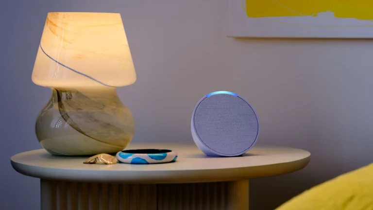 Amazon Echo Pop com Alexa sobre mesa ao lado de luminária em ambiente residencial