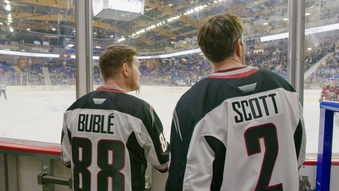 Michael Bublé e Drew Scott observam uma partida de hóquei com camisas do Vancouver Giants