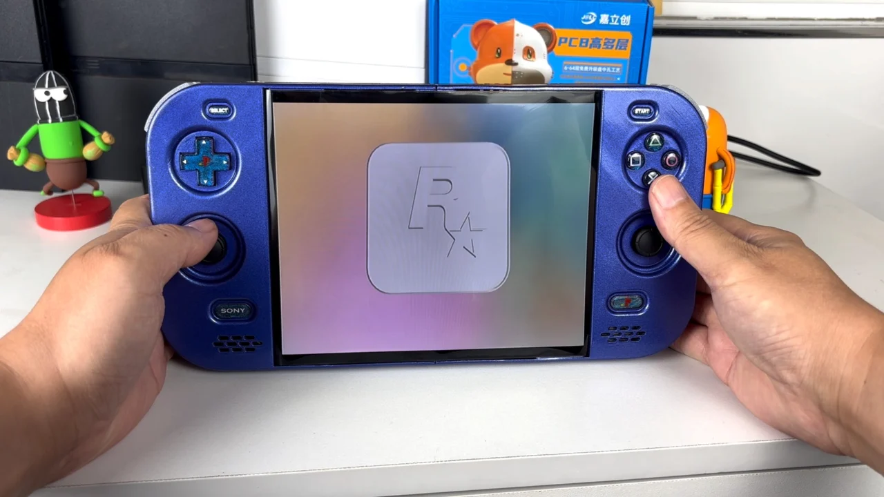PlayStation 2 DUO aberto sobre uma mesa, com carcaça roxa, controles integrados e tela exibindo uma animação de inicialização