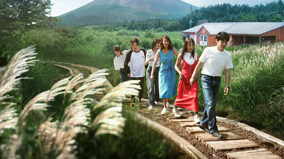 Participantes de Vilarejo do Amor caminham perto da casa vermelha da terceira temporada, com o Monte Fuji ao fundo