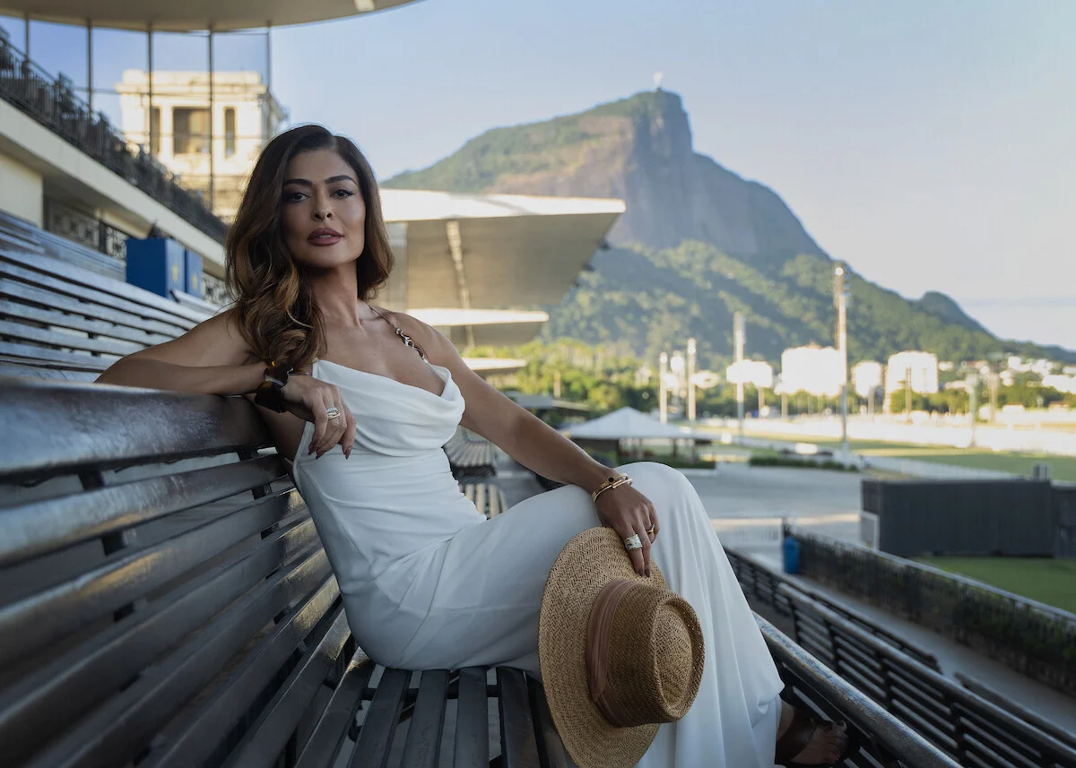Juliana Paes interpreta Leila em Os Donos do Jogo, sentada de vestido branco com a paisagem do Rio ao fundo
