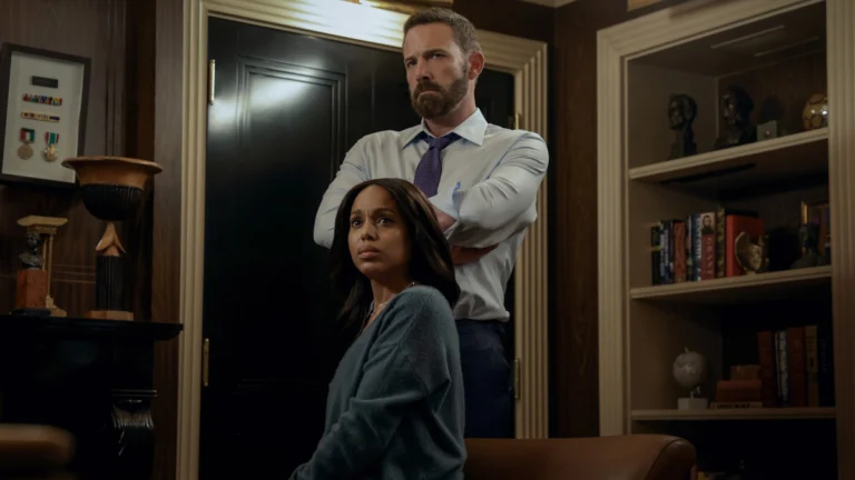 Mark em pé atrás de Abigail, sentada em uma sala com estantes, no filme Sobrevivência.