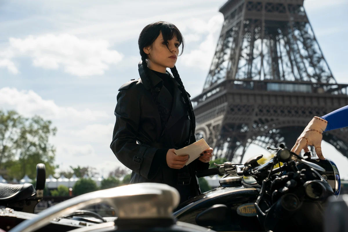 Jenna Ortega caracterizada como Wandinha diante da Torre Eiffel em Paris, em imagem oficial da terceira temporada