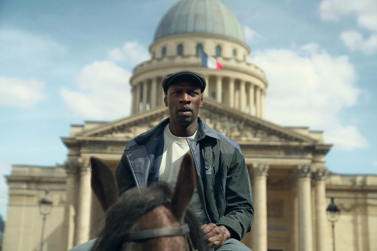 Assane Diop aparece montado em um cavalo diante de um monumento histórico de Paris na quarta parte de Lupin
