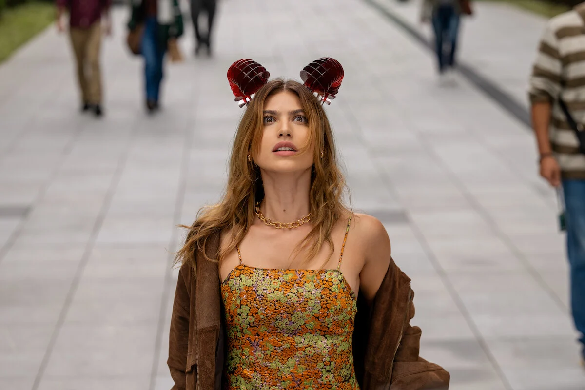Giovanna Grigio como Valentina usando um vestido floral e acessórios vermelhos em cena da série