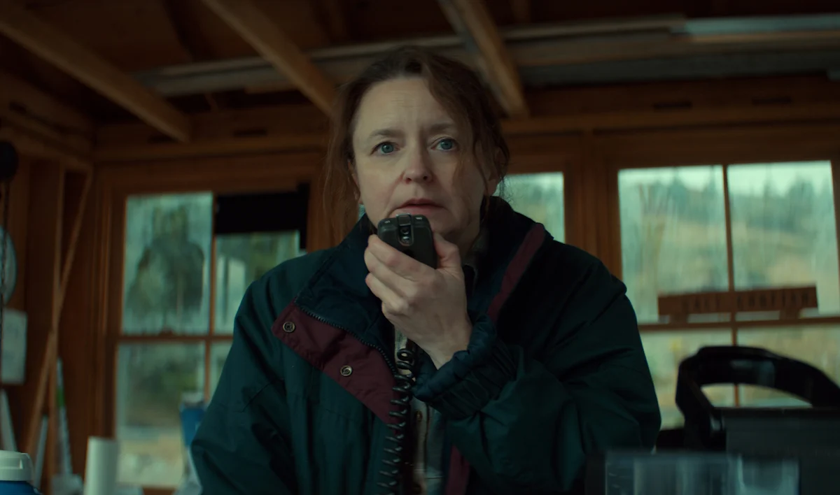 Willow Kean como Ruth Penney segurando um rádio comunicador no porto em Profundezas
