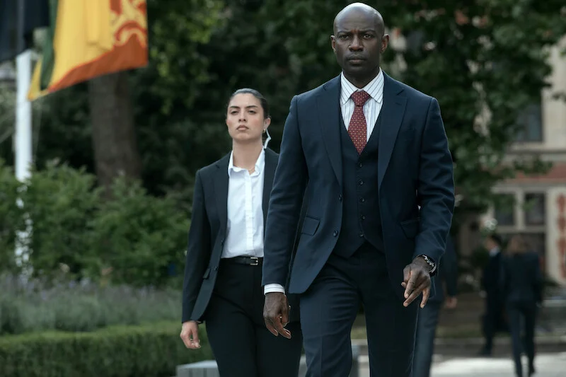 Austin Dennison, interpretado por David Gyasi, caminha em área externa em A Diplomata