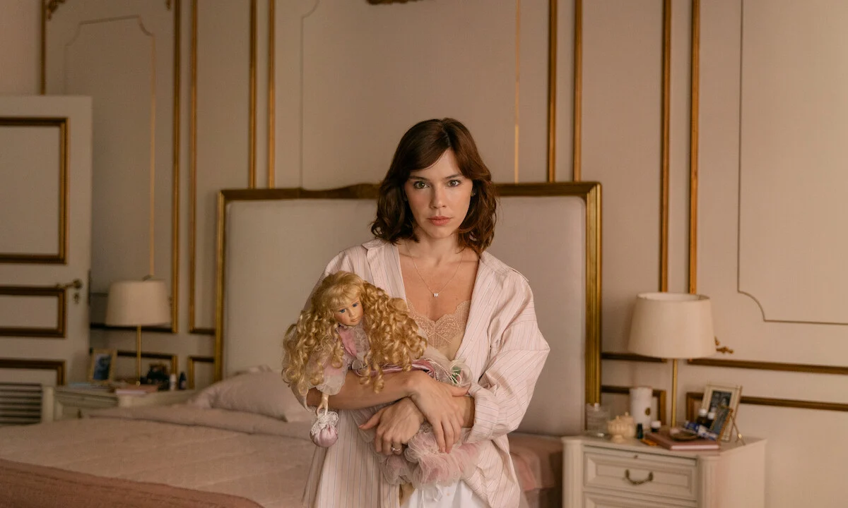 Alice Wegmann interpreta Maíra Rossetti segurando uma boneca no quarto da personagem na série Dom de Iludir
