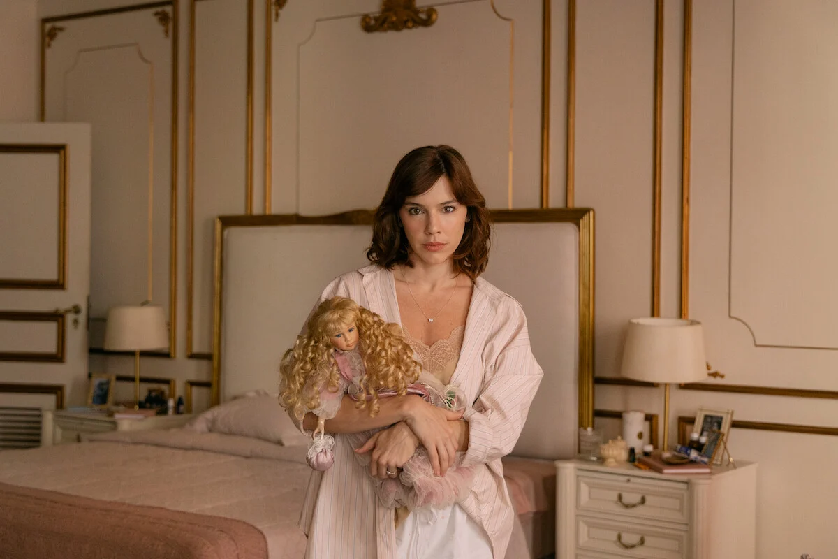 Alice Wegmann interpreta Maíra Rossetti segurando uma boneca no quarto da personagem na série Dom de Iludir