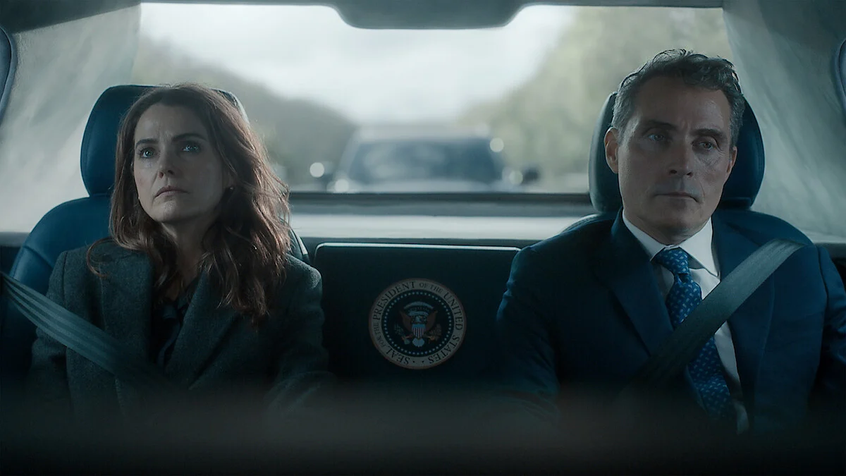 Keri Russell e Rufus Sewell em cena da quarta temporada de A Diplomata dentro de um automóvel oficial