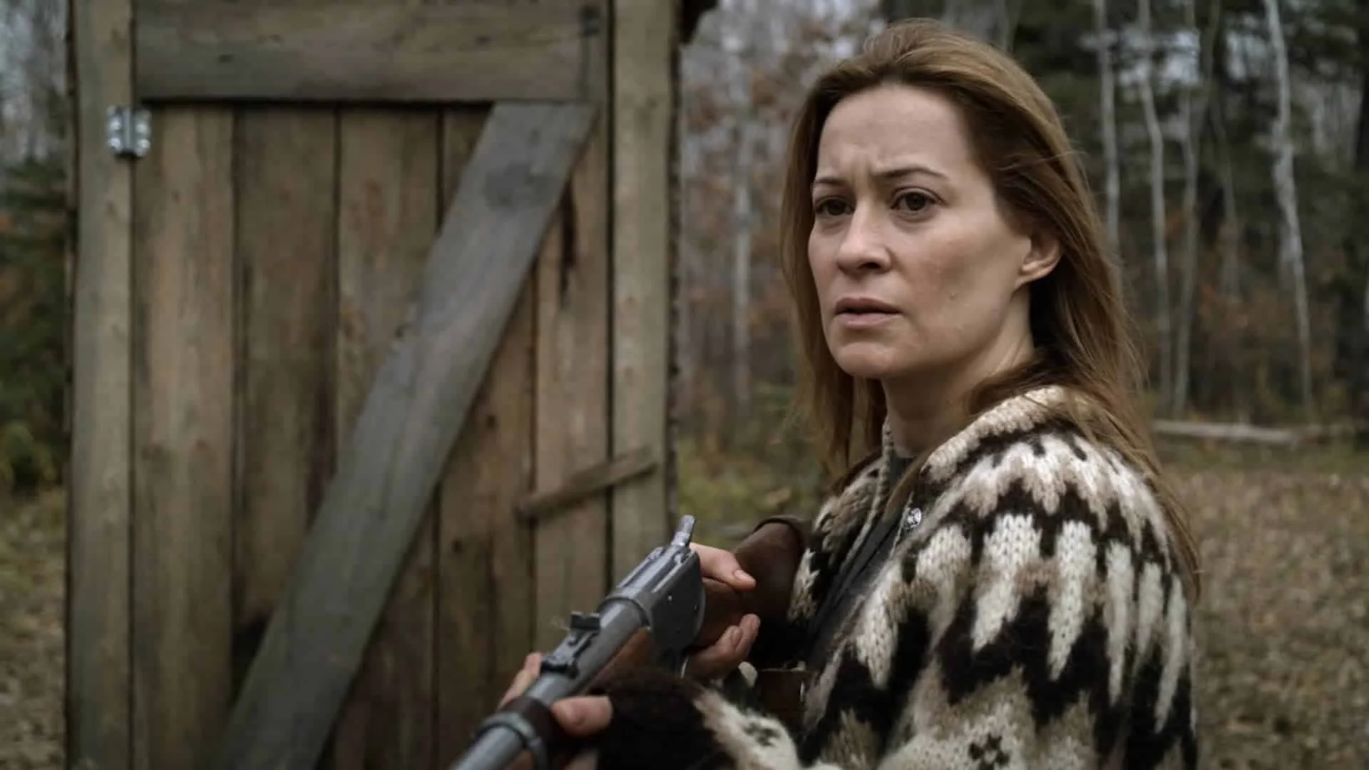 Camille Sullivan como Anne, com uma espingarda diante da cabana e da floresta em Caçada (2020)