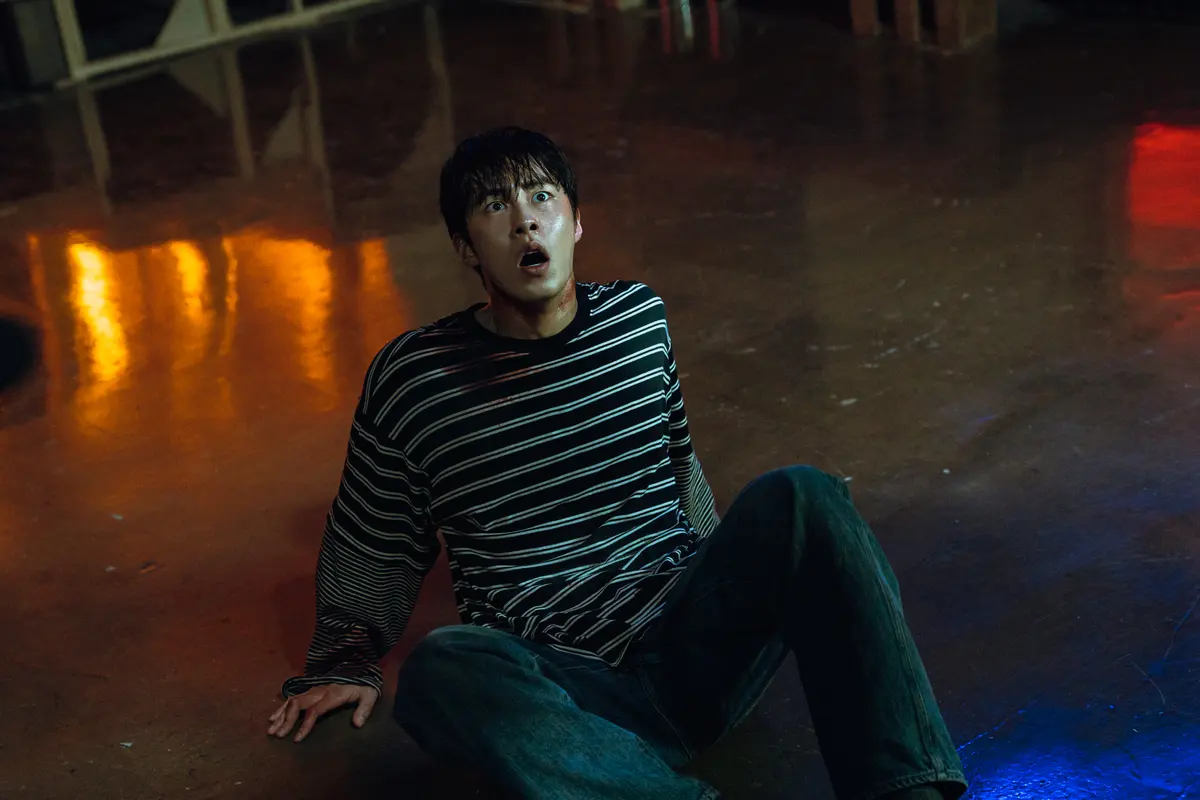 Lee Jae-wook como Hyeok-jun sentado no chão, assustado, em uma cena de Um Trabalho do Inferno