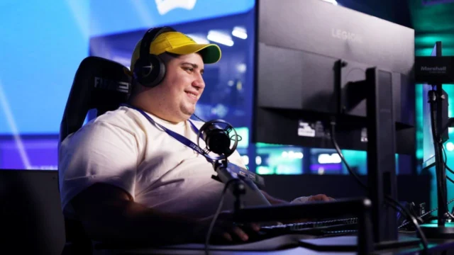 Dedeco usa headset e boné do Brasil diante de um computador e um microfone