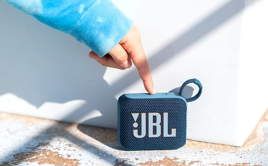 Caixa de som JBL Go 4 azul apoiada em uma superfície, com alça e botões de controle