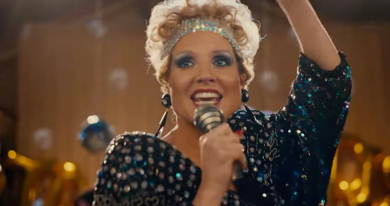 Jessica Chastain caracterizada como Tammy Faye Bakker canta diante de um microfone