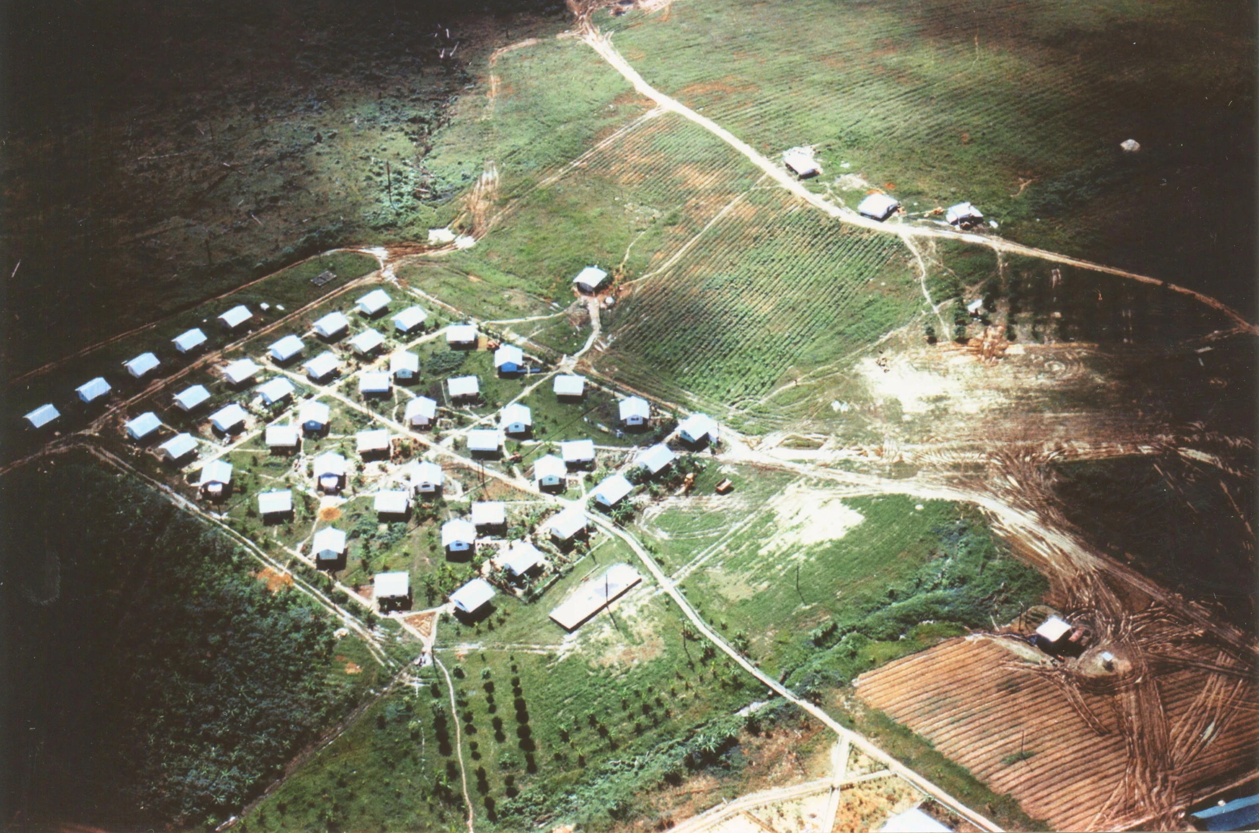Vista aérea histórica da comunidade de Jonestown na Guiana, com casas e plantações cercadas pela floresta