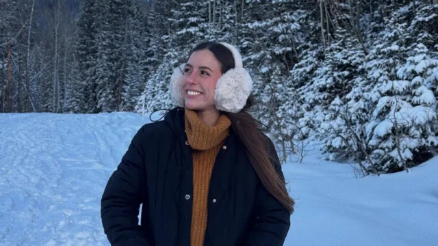 Renata Alves Mietto com casaco e protetores de orelha diante de uma paisagem coberta de neve