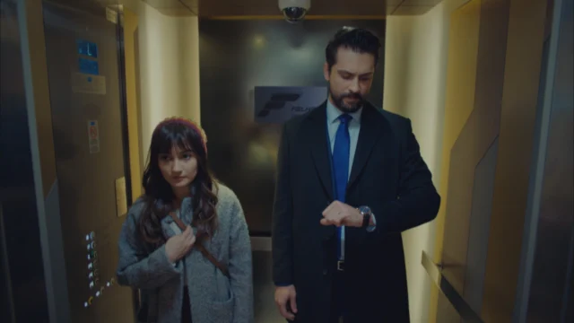 Alihan, interpretado por Onur Tuna, olha para o relógio enquanto Zeynep está ao seu lado em um elevador