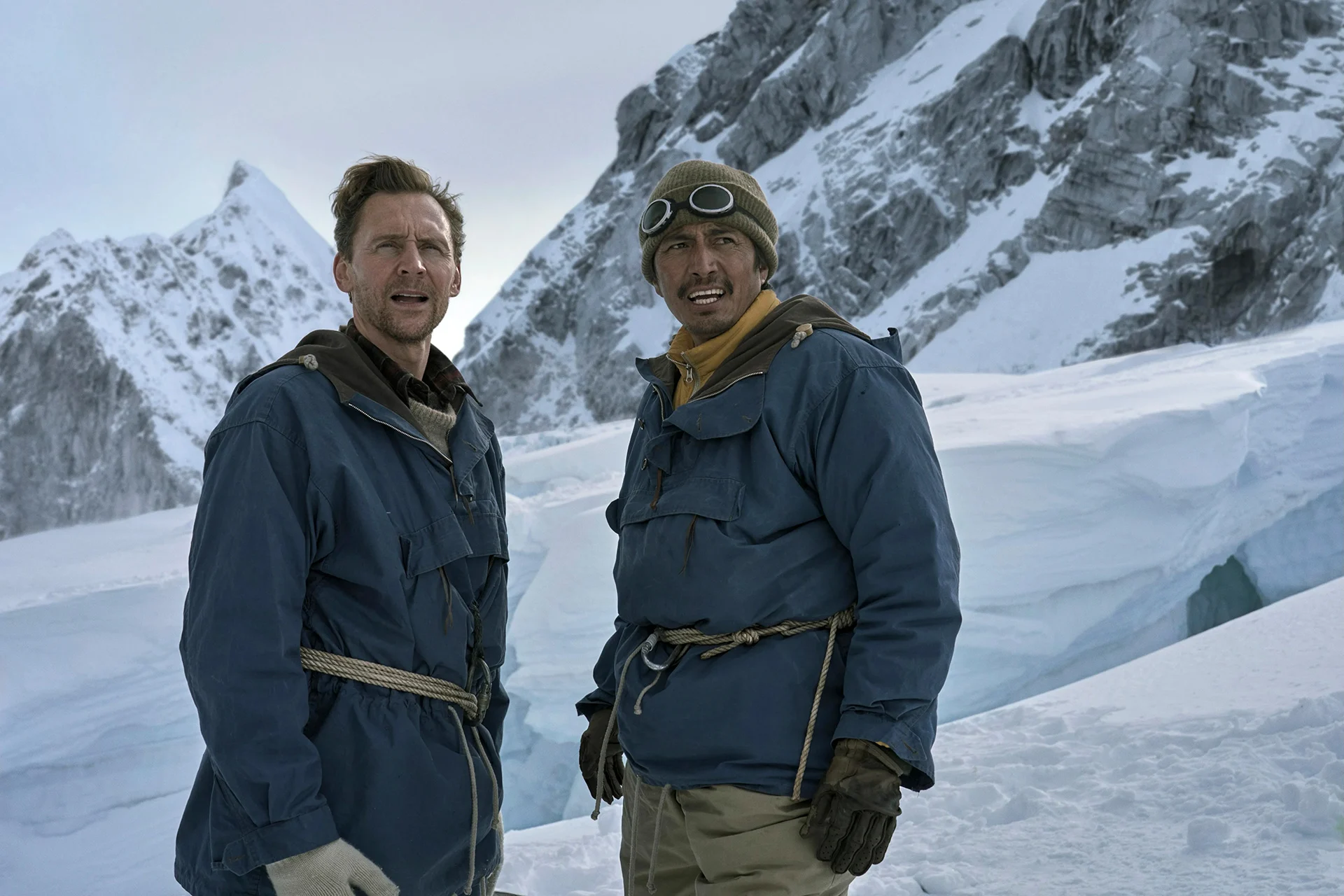 Tom Hiddleston e Genden Phuntsok em roupas de alpinismo sobre uma montanha nevada no filme Tenzing