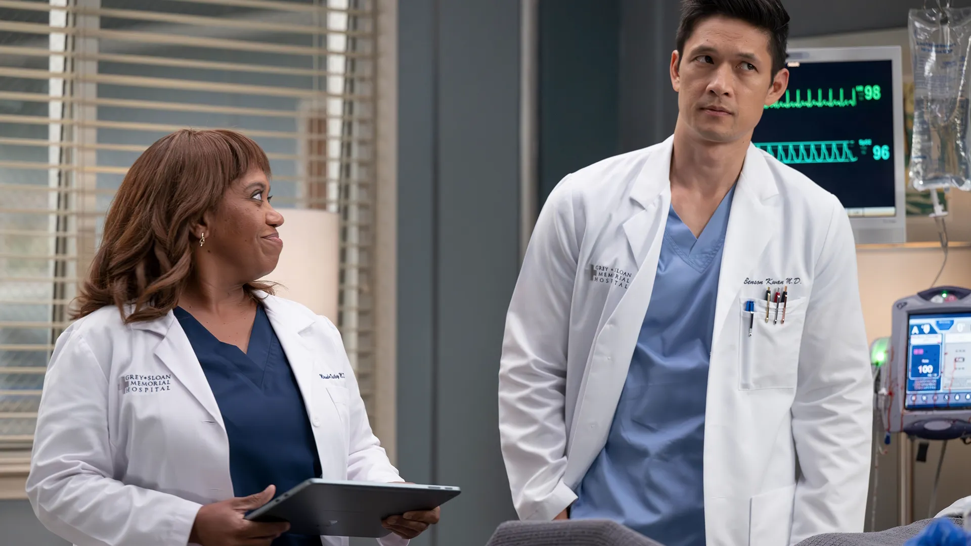Dois médicos de jaleco ao lado de um leito hospitalar em cena da temporada 22 de Grey’s Anatomy.